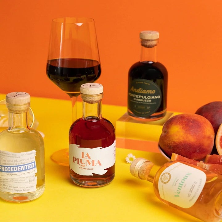 four bottles of wine, a glass of red wine, and peaches in a bowl