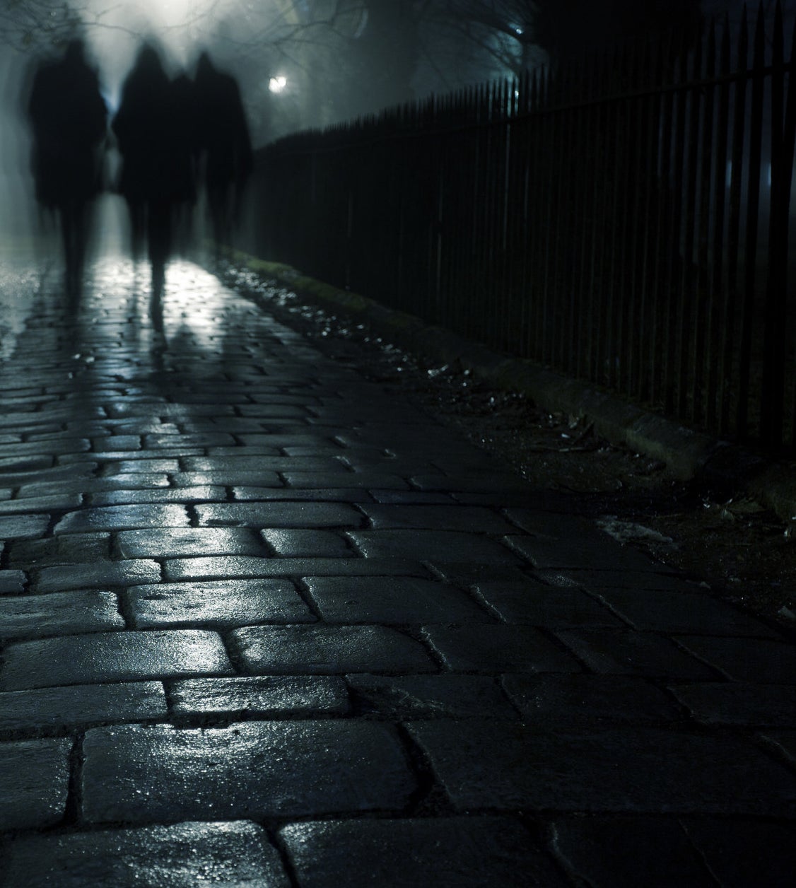 Three people walking on a dark sidewalk in the evening fog