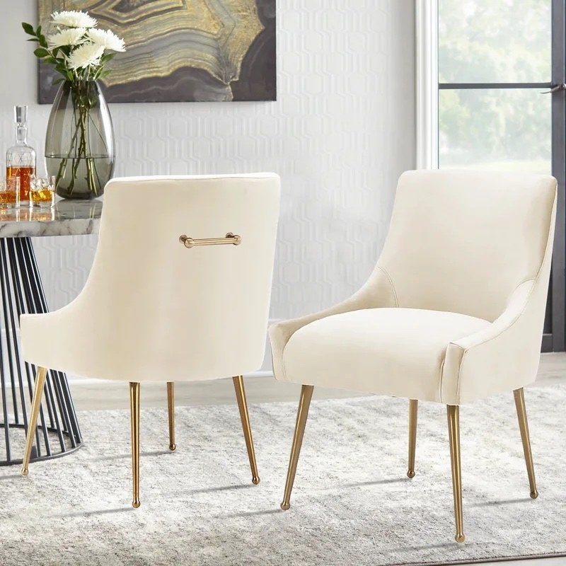 two white velvet dining chairs with gold accents next to a dining table