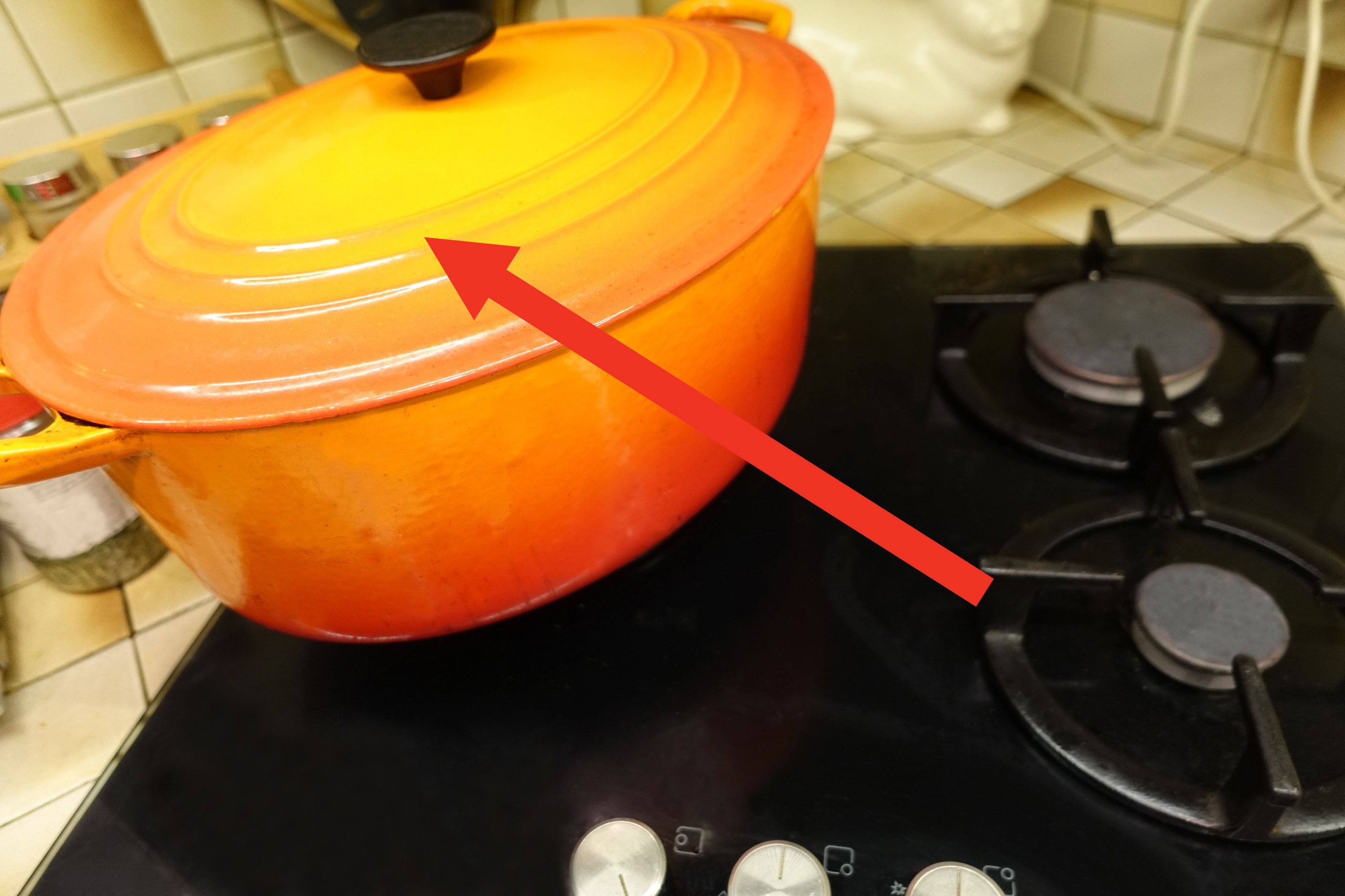 A Dutch oven on a stove with an arrow pointing to the lid