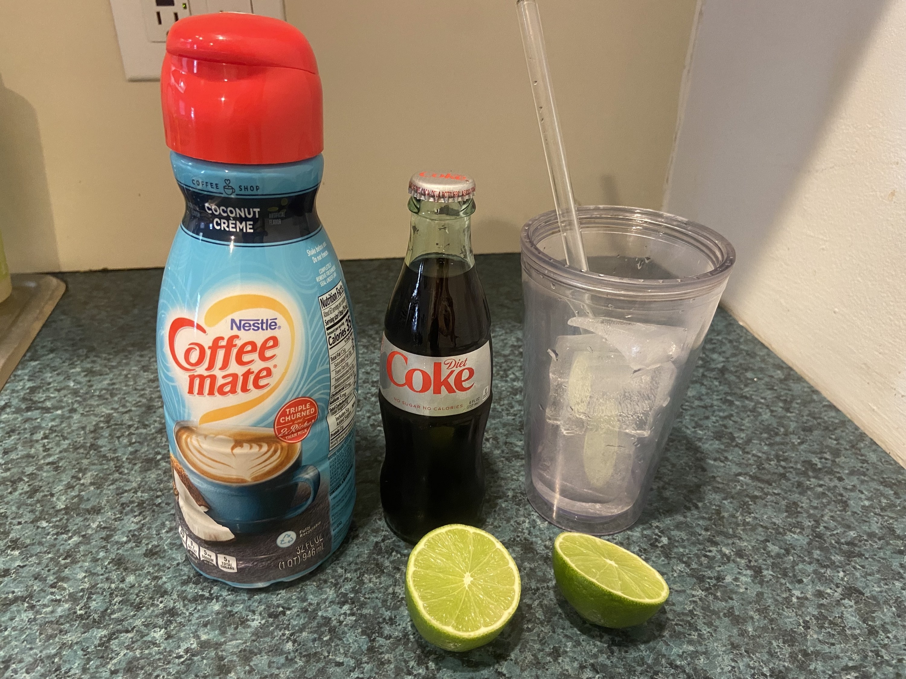Creamer, Diet Coke, a cup with ice, and a lime cut in half on a countertop