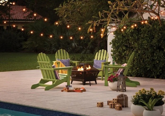 string lights over green chairs around fire pit on a patio