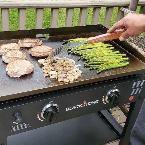 person cooking meat and veggies on griddle