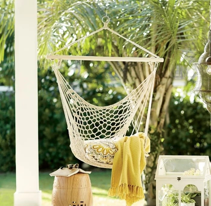 woven hammock chair with pillow and yellow blanket suspended from covered patio