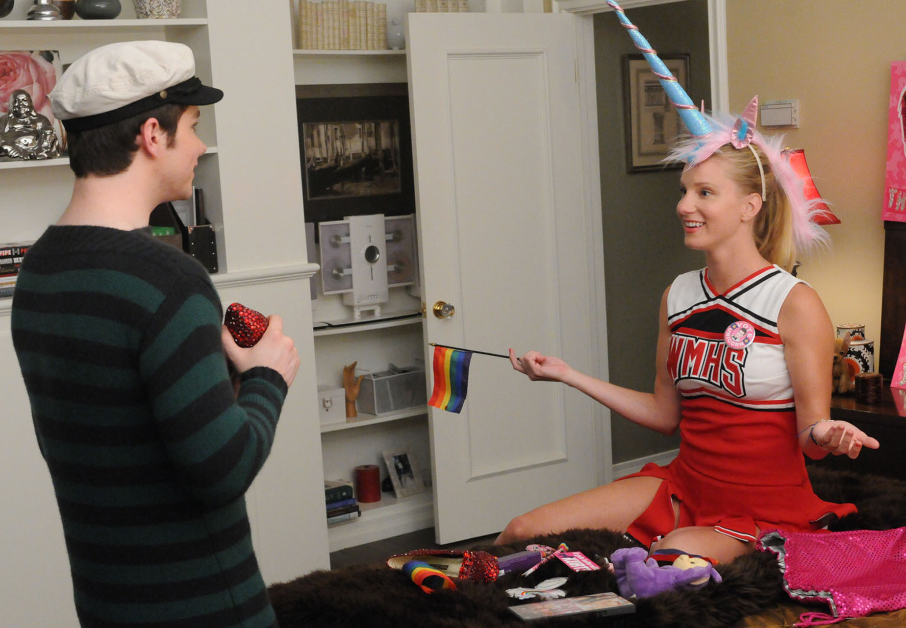 Criss and Morris in character in a room while Morris wear the cheer uniform and a unicorn horn headband