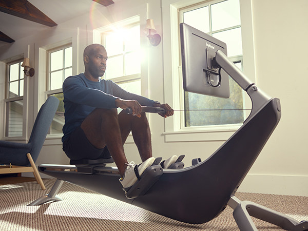 Man sitting on a Hydrow Rowing Machine in his living room, preparing to exercise