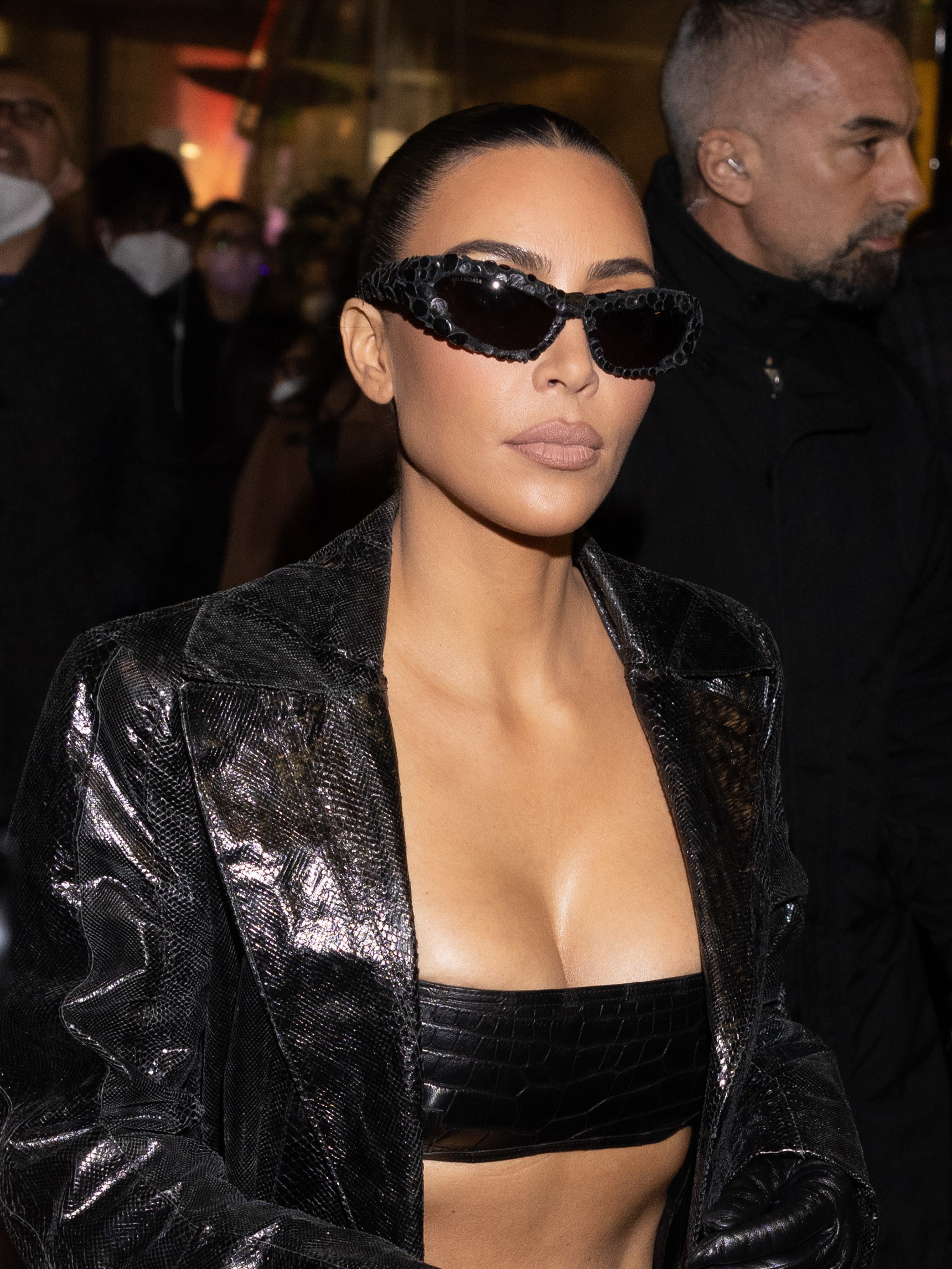 Kim walks in a coat, top, and sunglasses