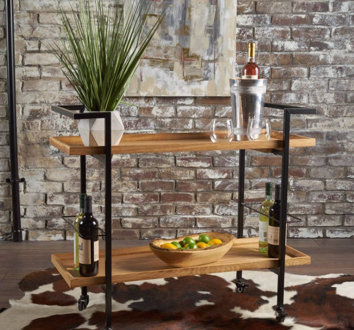 A two-shelf bar cart with black frame and light brown wooden shelves atop a cow skin rug.