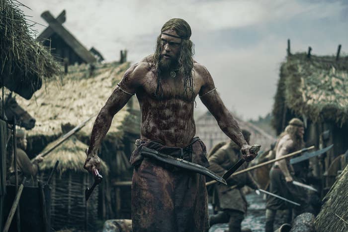 Alexander Skarsgård holds an axe and a sword in his hands standing in a Slavic village in 10th century