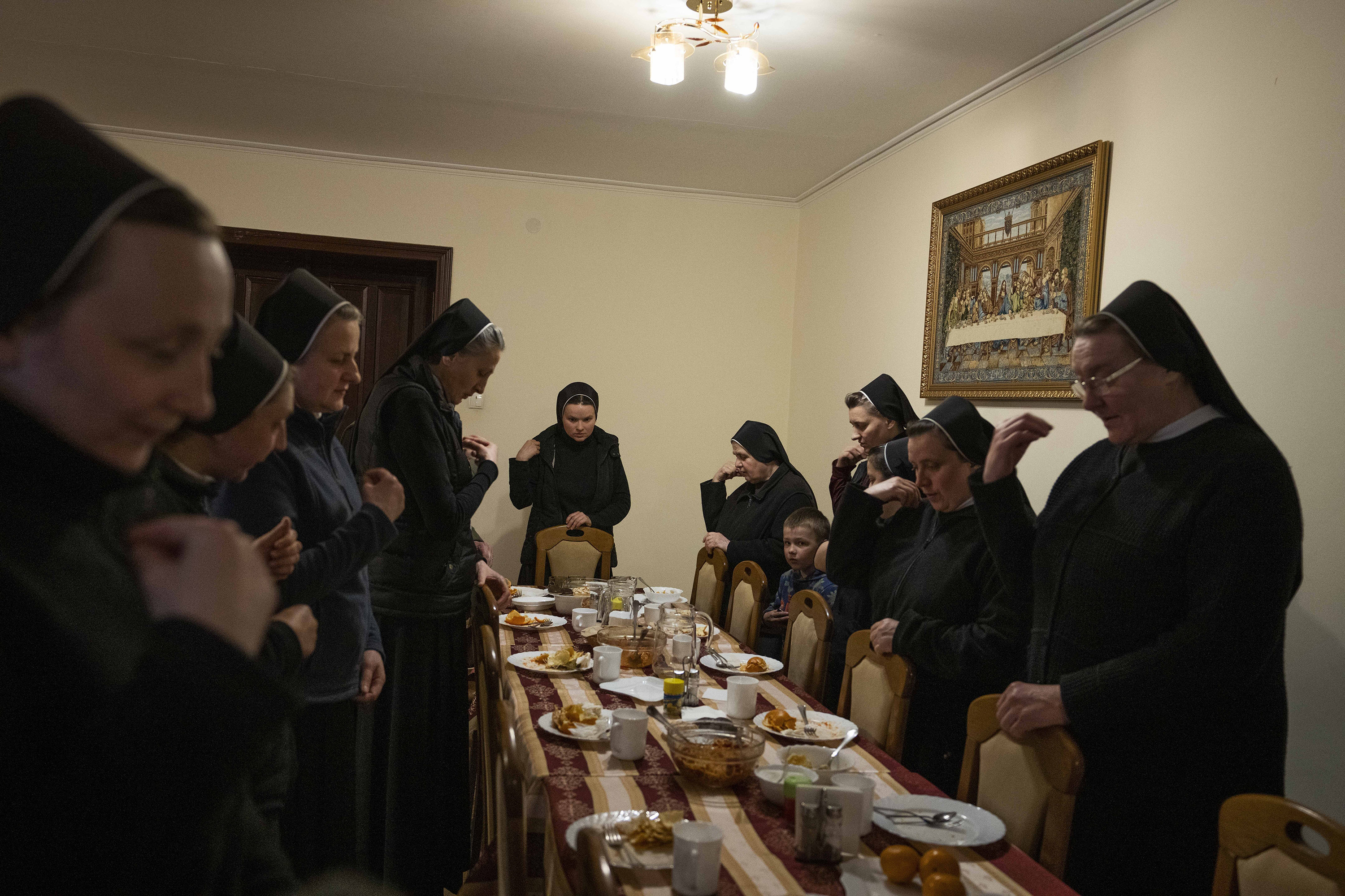 Nuns with their heads bowed stand around a long dining table