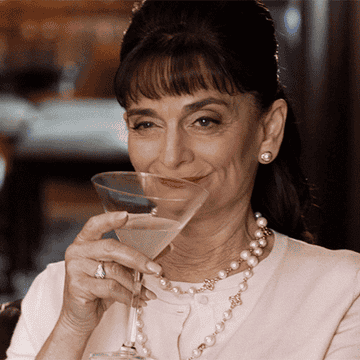 A woman wearing nice jewelry and sipping a drink from a martini glass