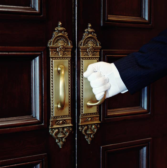 A butler&#x27;s gloved hand opening a door