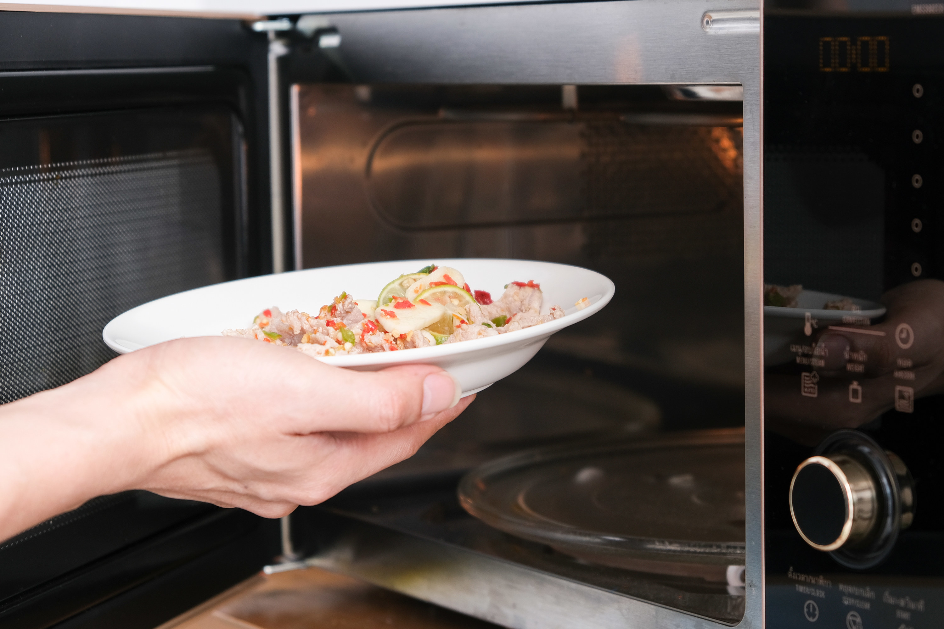 A person&#x27;s hands holding a bowl of food and putting it in the microwave