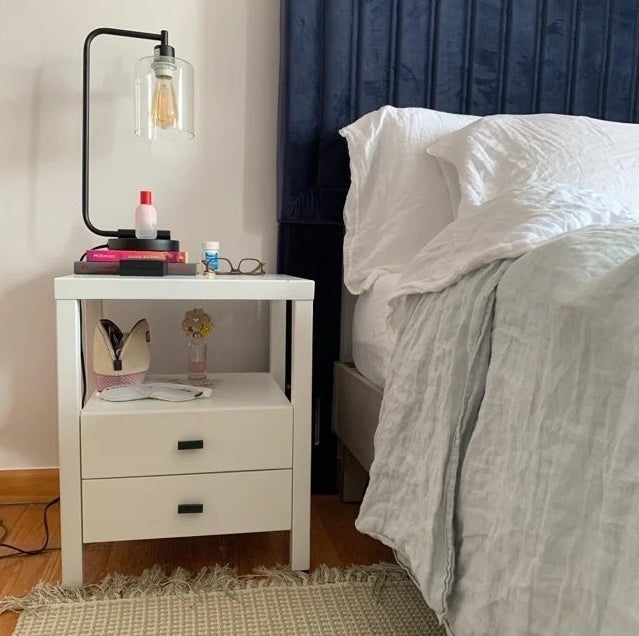 A white nightstand with two drawers and a shelf in a bedroom