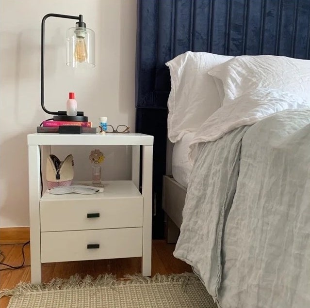 A white nightstand with two drawers and a shelf in a bedroom