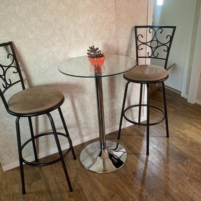 A bar height glass table with chrome base and two tall chairs
