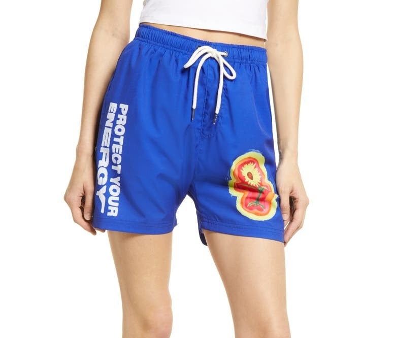A person wearing the shorts, which have a flower on one leg and "protect your energy" written on the other