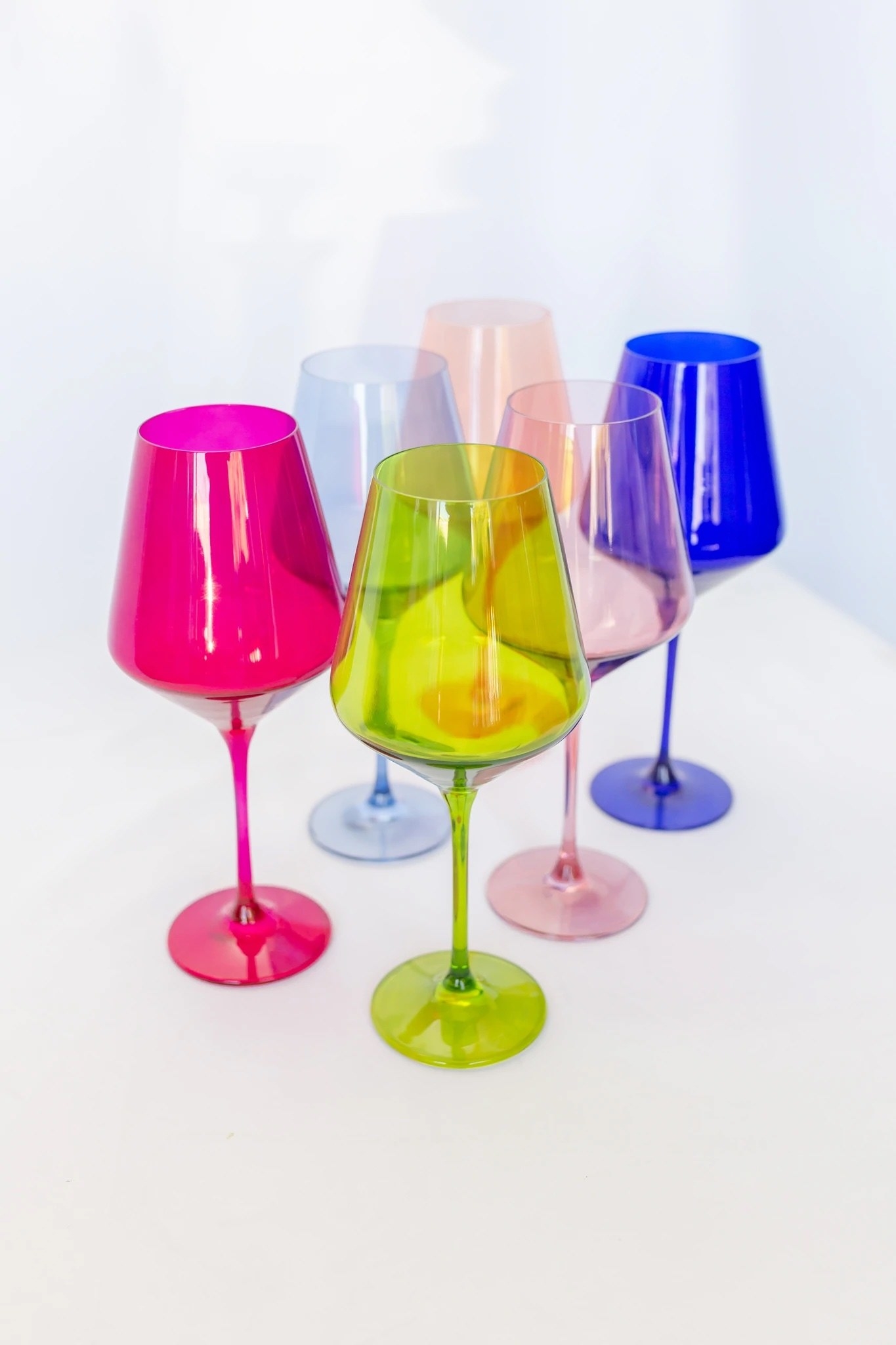 Six wine glasses; one in green, hot pink, light pink, light blue, peach, and dark blue