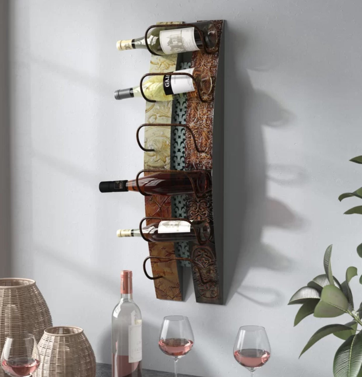 The wine rack mounted on a wall, holding four bottles of wine with two empty holders