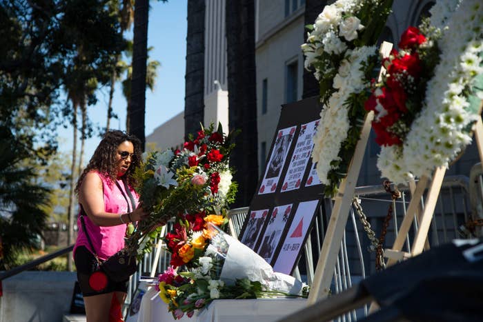 A person adds to the flowers on a coffin in front of placards on a table