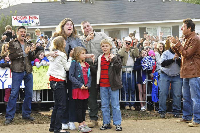 a family with a crowd of neighbors behind them as they look at their new house