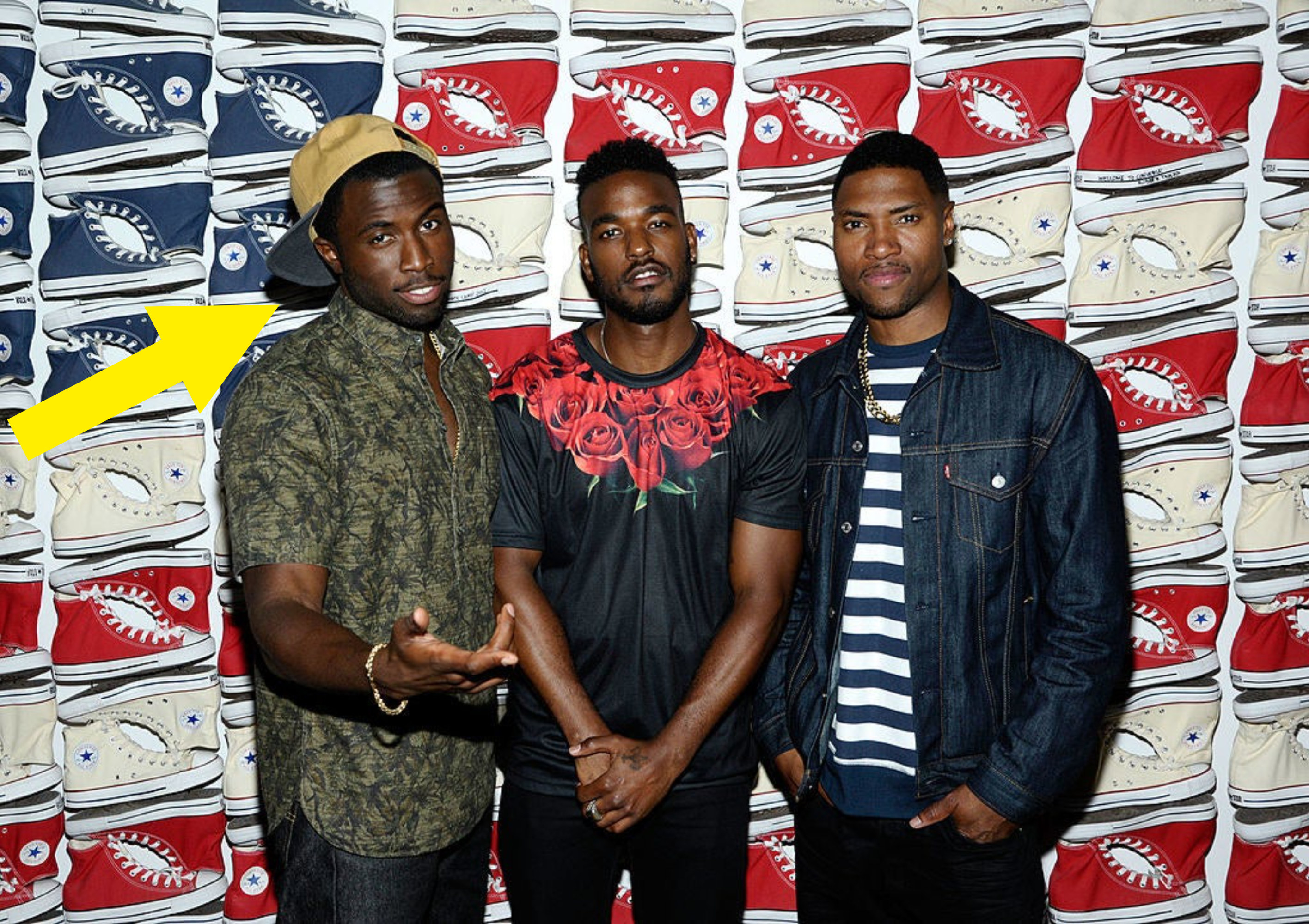 Y&#x27;lan Noel standing in front of a backdrop of rows of Converse shoes with two other guys