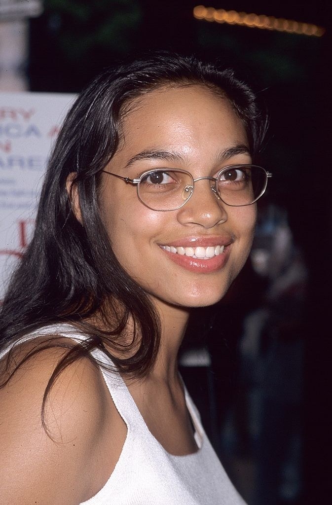 A young Rosario Dawson wearing glasses and smiling