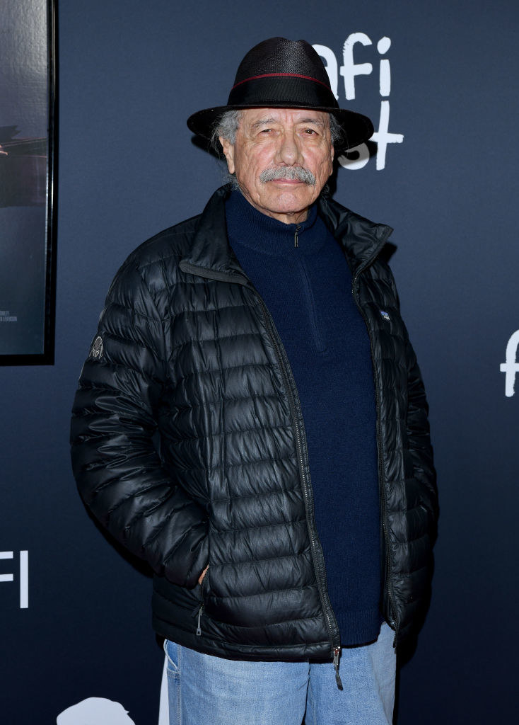 Edward James Olmos with his hands in his pockets wearing a fedora and looking serious