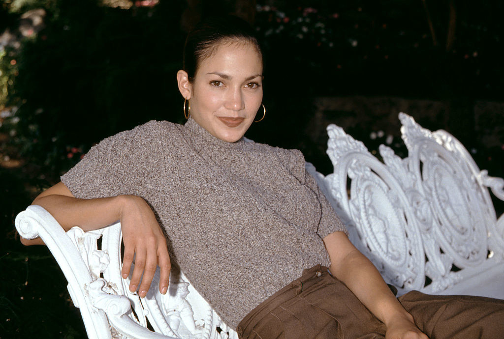 Jennifer Lopez lounging on a park bench and smiling