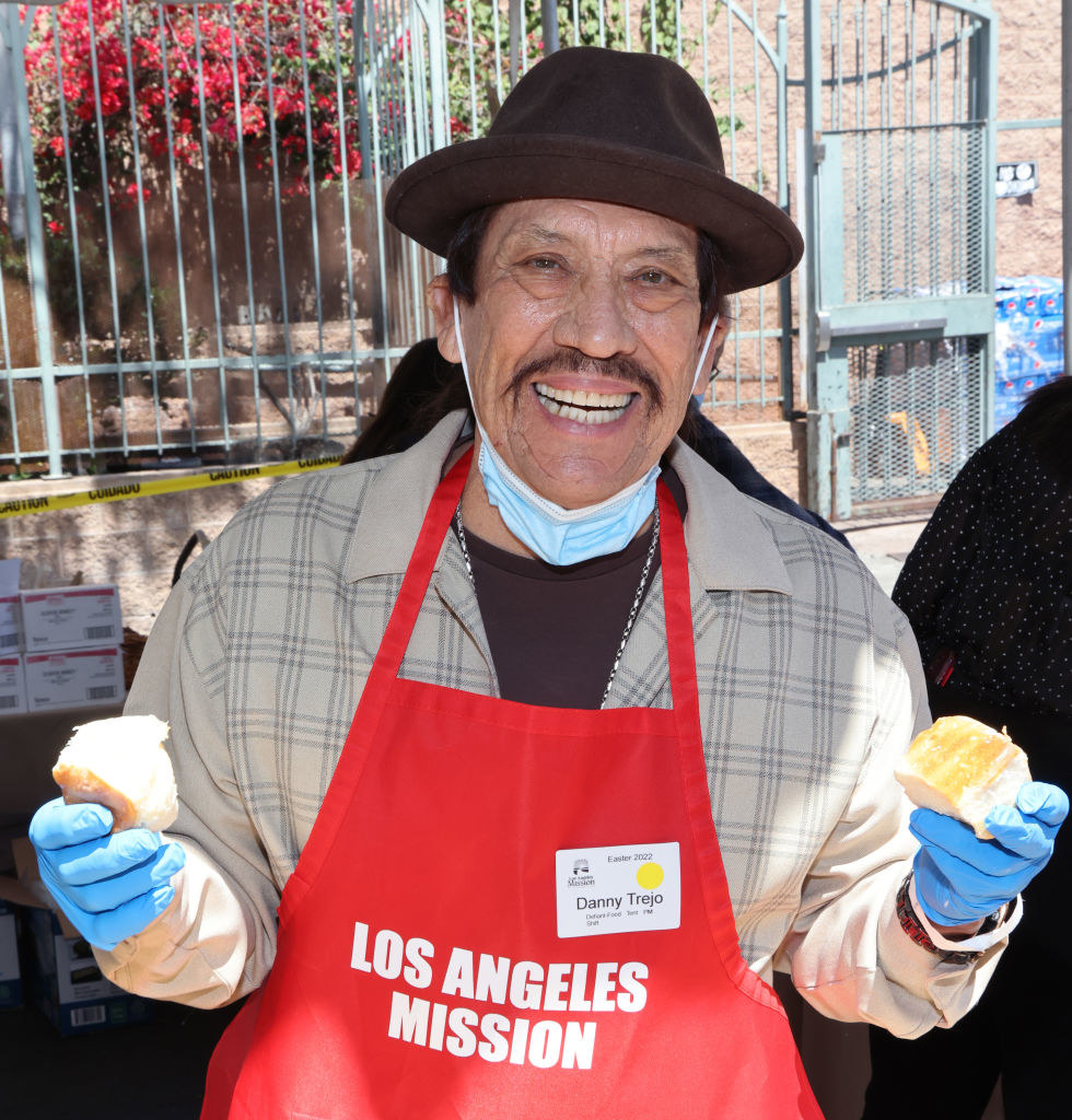 Danny Trejo smiling, holding food, and wearing a Los Angeles Mission apron