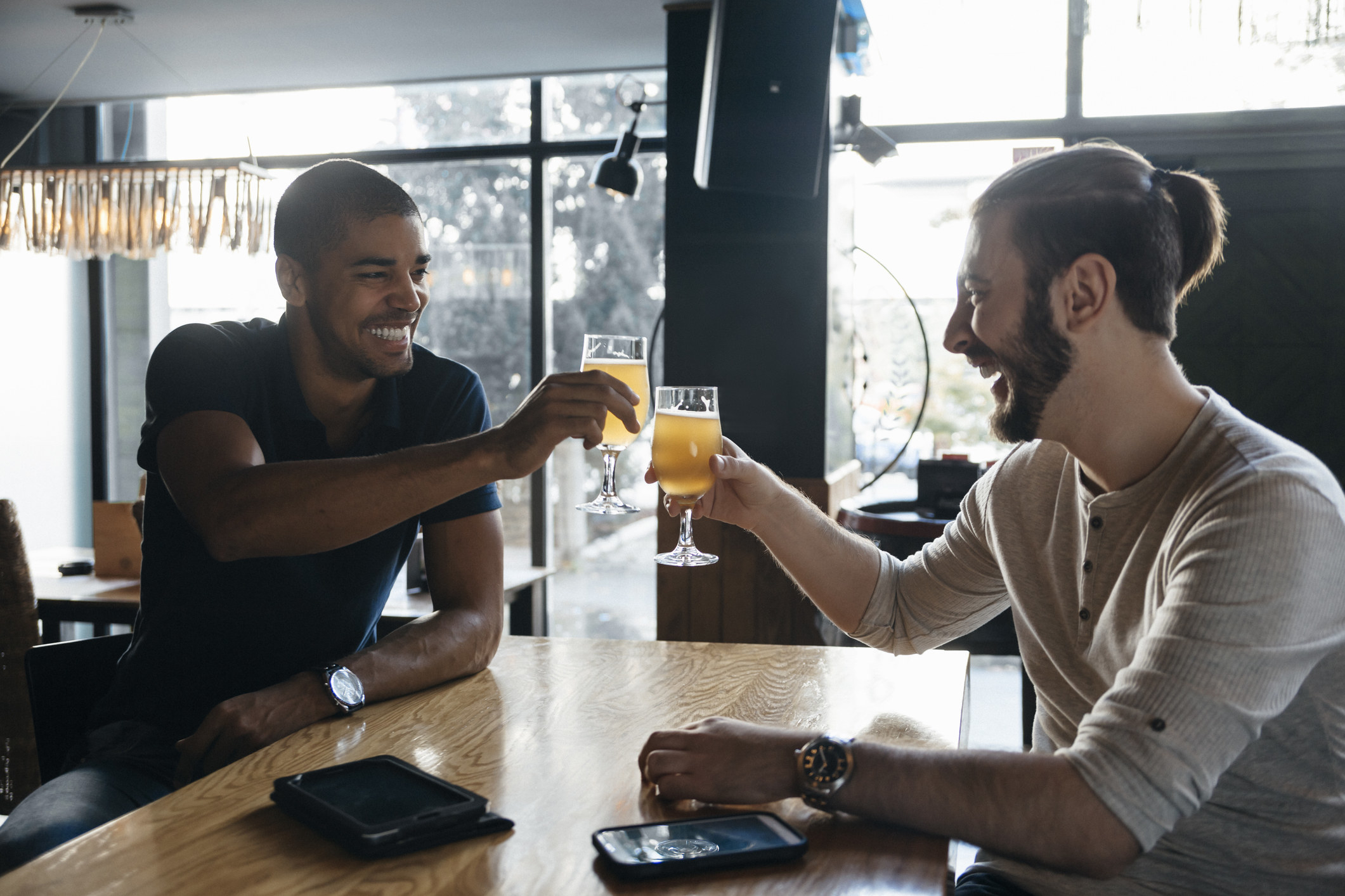 Two men smiling and saying cheers in a bar.