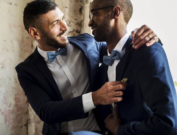 Two men in tuxedos embracing and smiling.