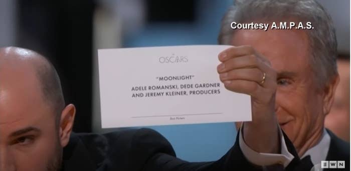 A man holds a piece of paper with &quot;Moonlight&quot; written on it up to the camera, looking serious