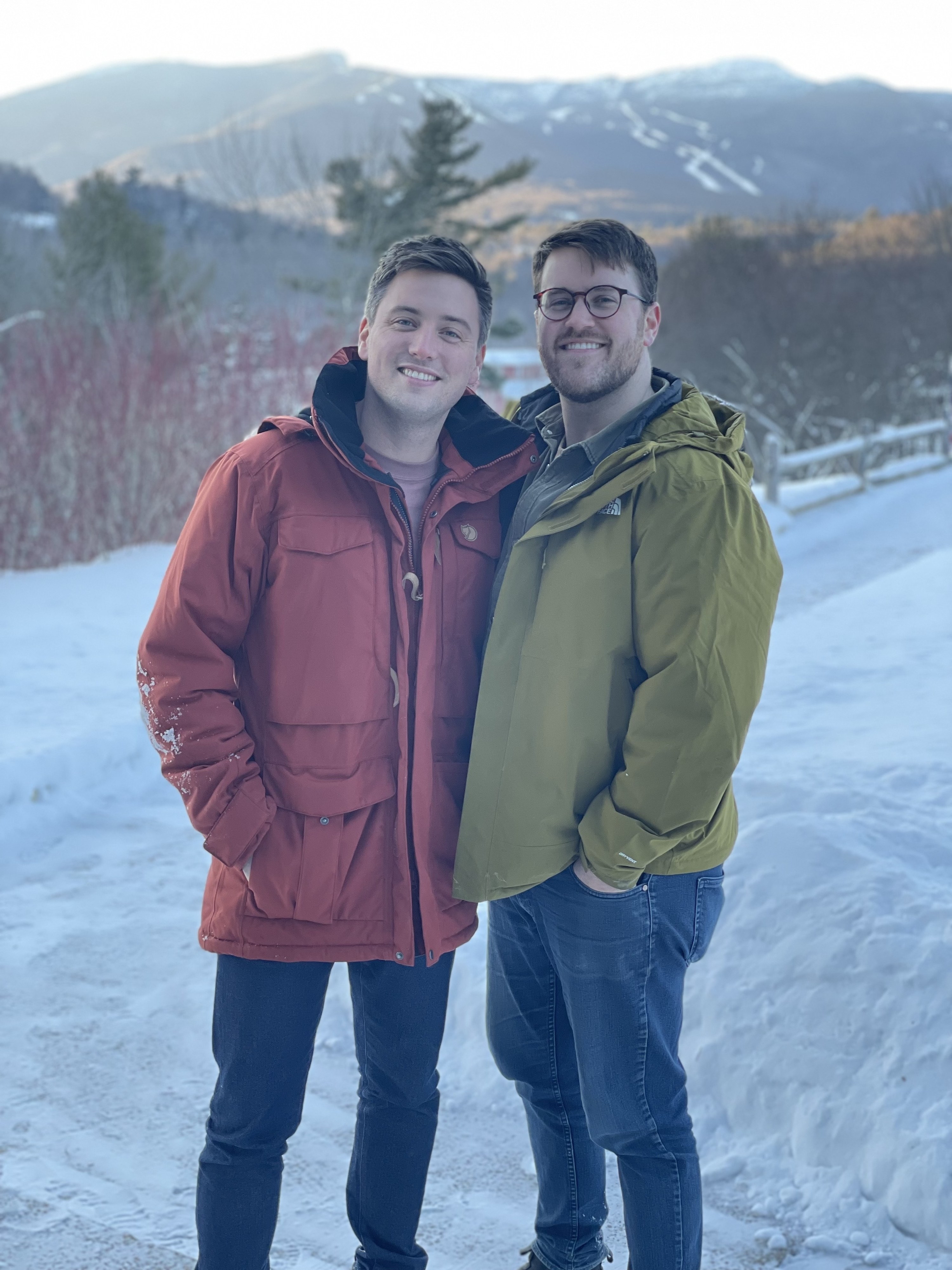 Two people wearing jeans and jackets stand together in a snowy setting