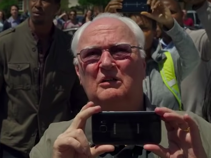 Close-up of Jim holding up a phone in a crowd