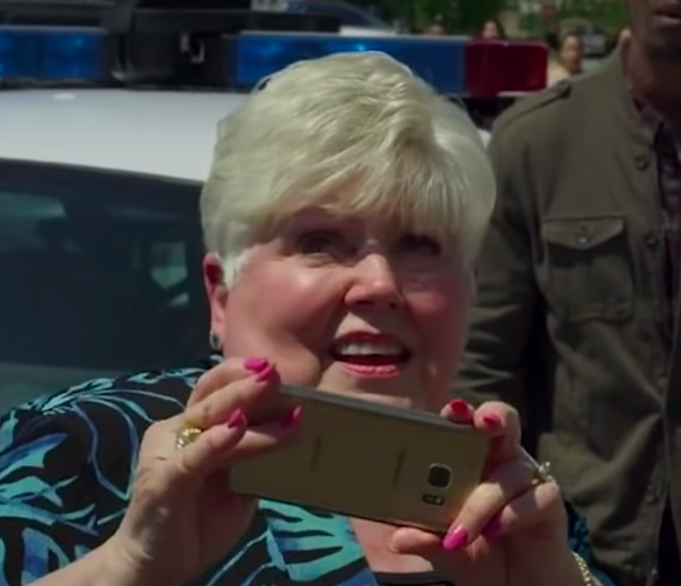 Close-up of Leota smiling and holding up a phone