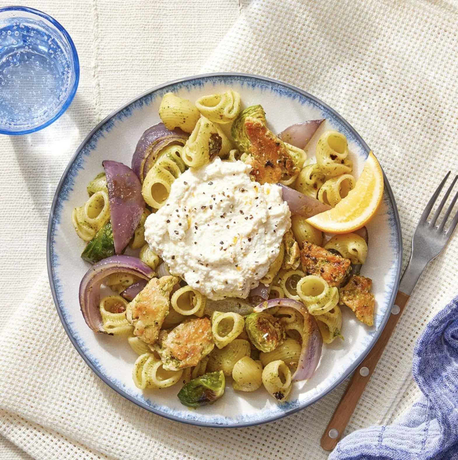 Pesto chicken pasta with red onions, ricotta, Brussels sprouts, and lemon on top