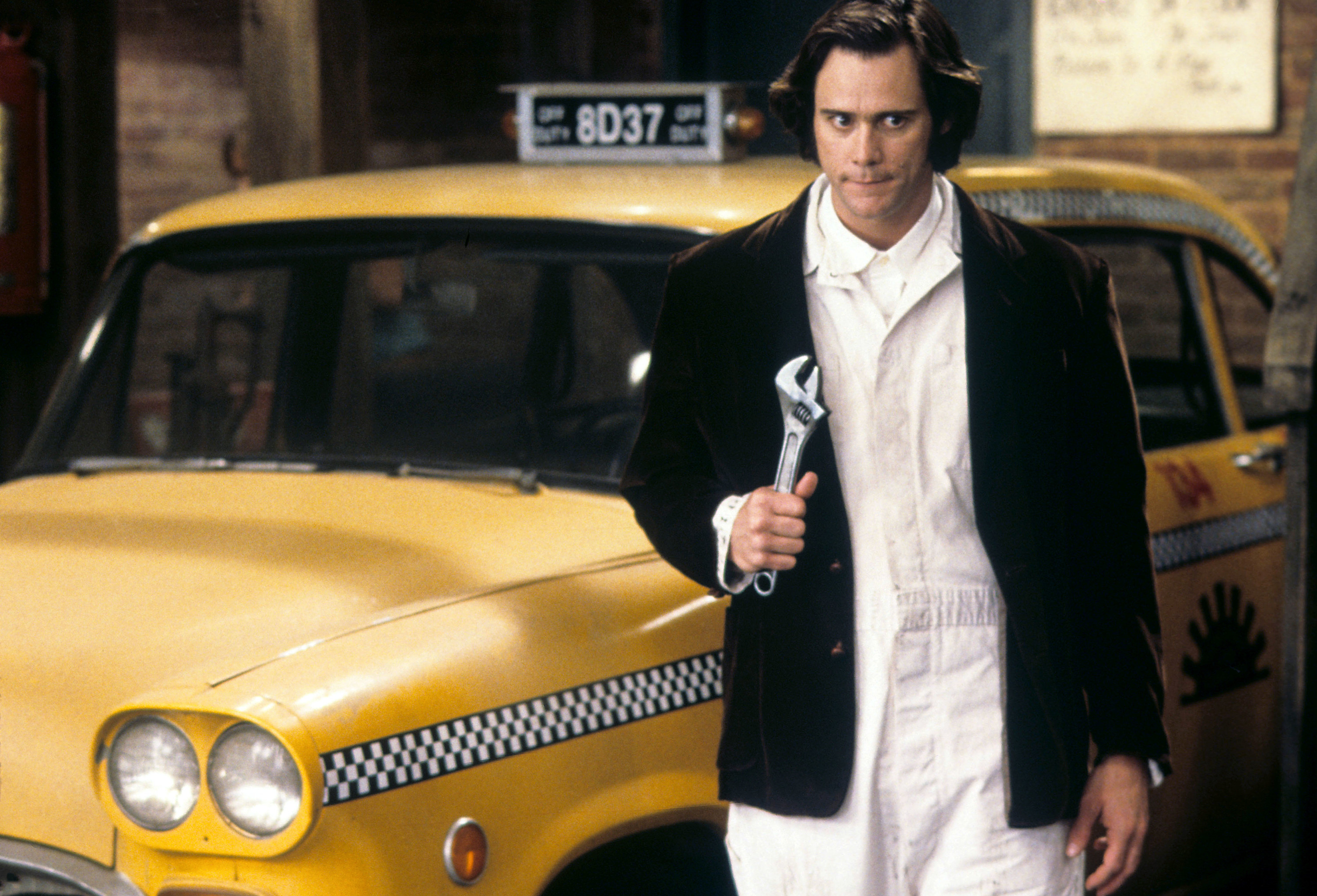 Jim Carrey as Andy Kaufman holding a wrench and standing by a cab