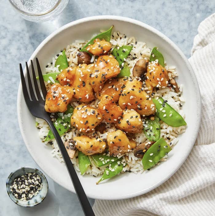 Soy and butter-glazed chicken over rice and snap peas and topped with sesame seeds