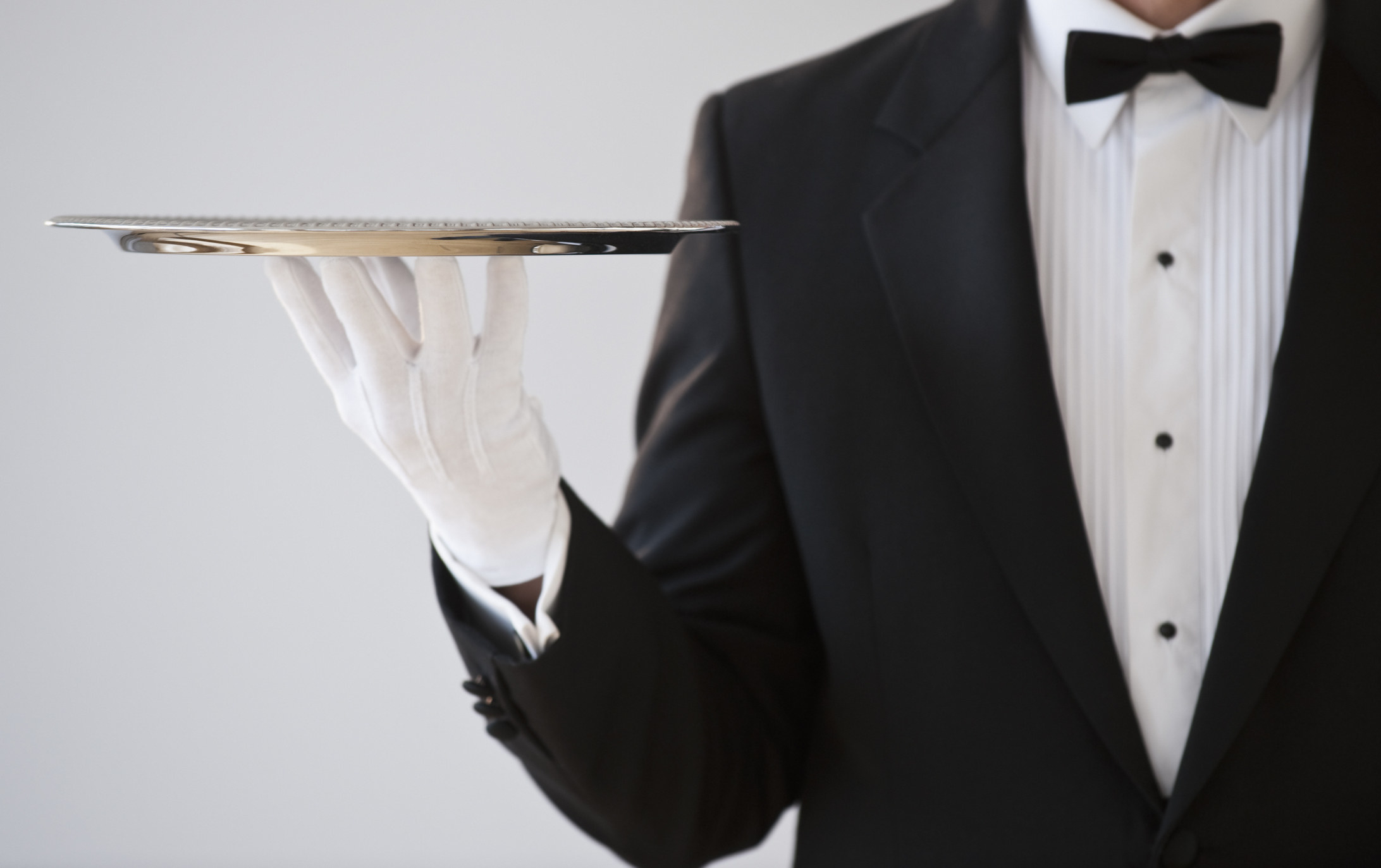 A person in a tuxedo and gloves holding a silver serving tray