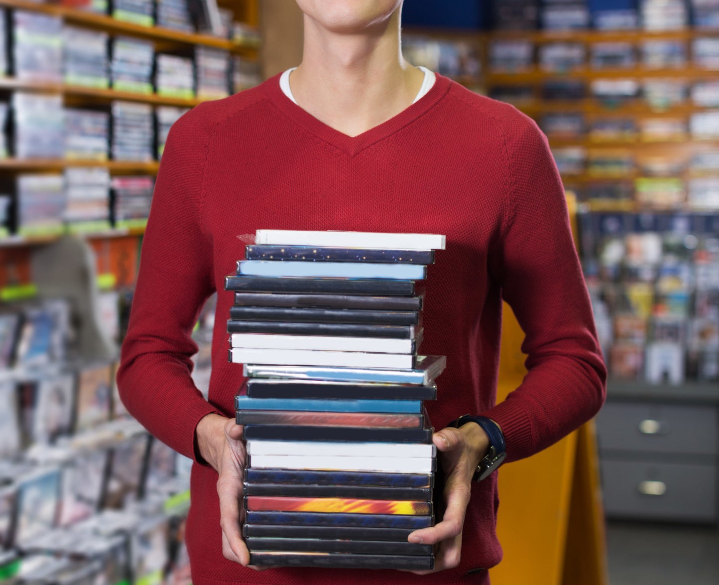 A person holding a stack of DVDs in a rental store