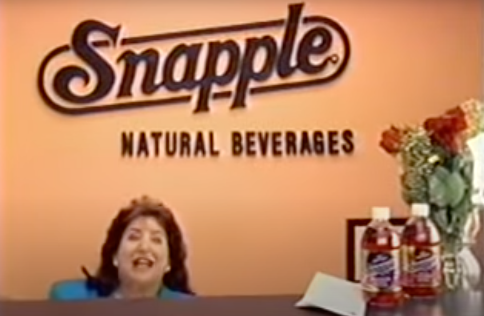 A lady behind a receptionist desk and a Snapple logo on the wall