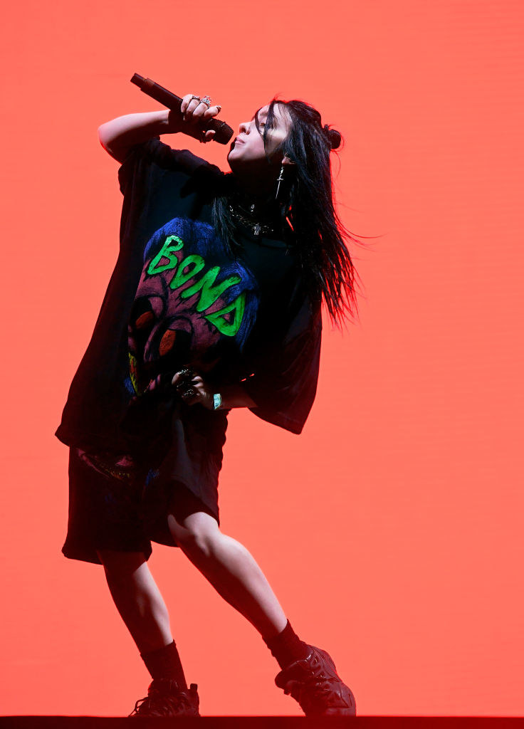 Billie Eilish performing onstage in an oversized t-shirt and shorts