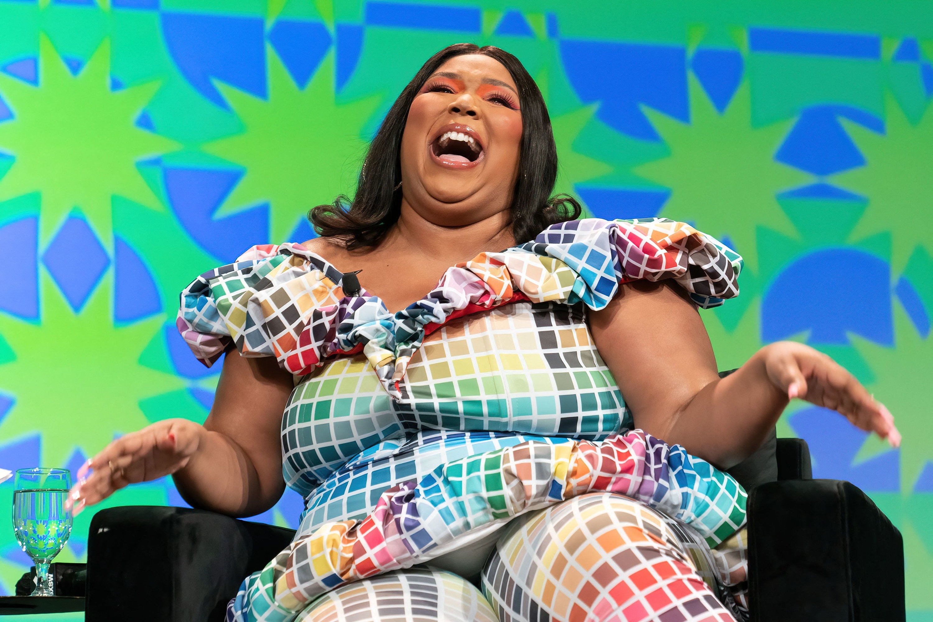 Lizzo laughs while sitting in a chair