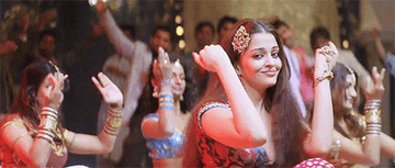 aishwarya dances, wearing metal gold clips in her hair, long gold earrings, gold bracelet connected to a ring