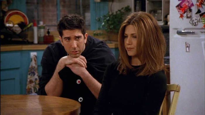 Ross Geller rests his chin on his hands as he looks at Rachel Green