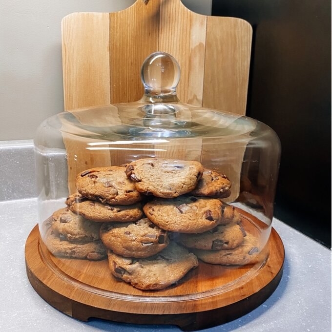 The clear white dome has a small knob on top and a bottom wooden tray filled with small cookies