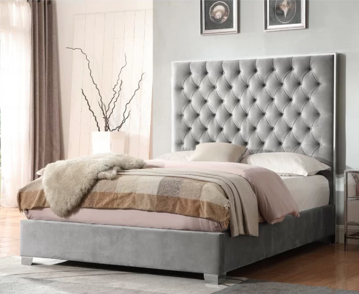 a grey velvet bed with a tall headboard and full base decorated with bedding in a staged bedroom