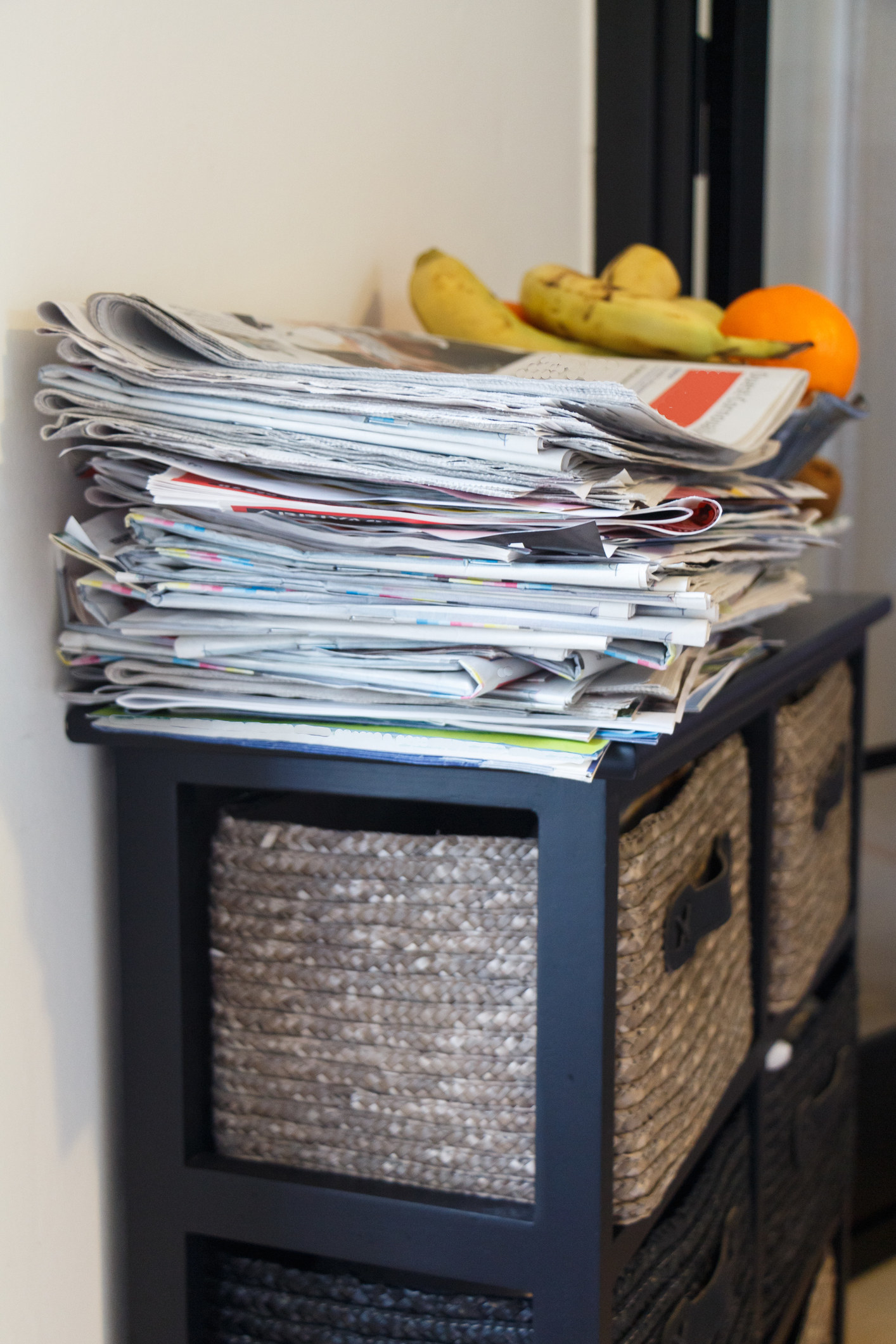 A stack of newspapers, topped by bananas, atop pullout drawers