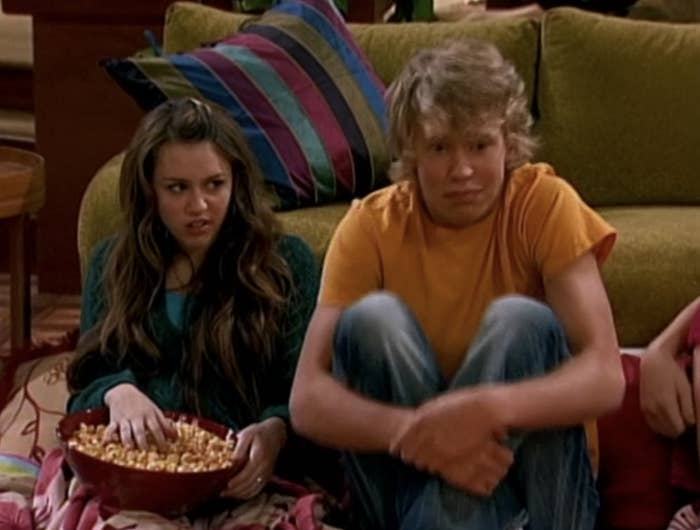 Miley Stewart sits on the floor next to Derek Hanson who looks scared
